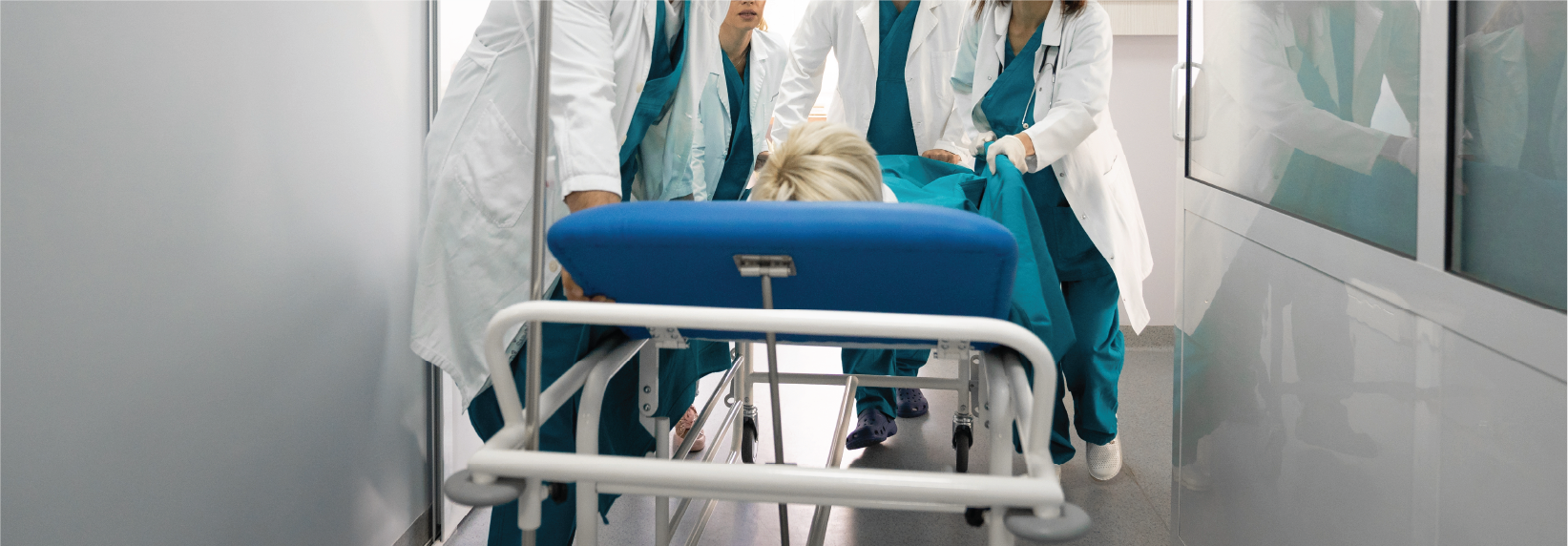 A medical team of healthcare professionals in scrubs and lab coats urgently assisting a patient on a stretcher in a hospital hallway. The team is working together to transport the patient, with a focused and coordinated approach.